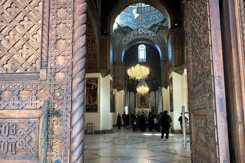 ورودی کلیسای جامع اچمیادزین، اولین کلیسای جامع جهان، با درهای چوبی منبت‌کاری شده و چلچراغ‌های باشکوه