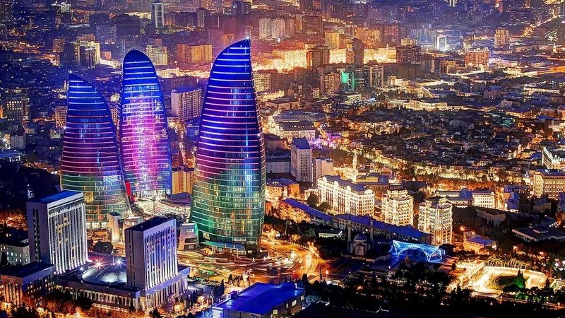 یک منظرۀ شهری شبانه از برج‌های شعلۀ باکو (Flame Towers) با نورپردازی آبی و بنفش. 